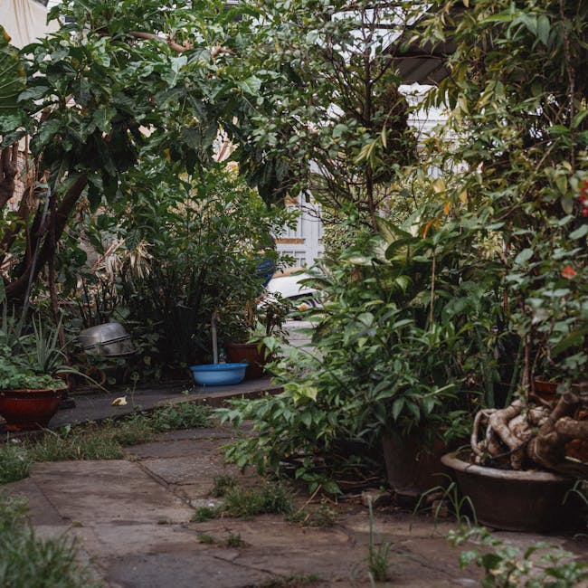 A person wearing a white gardening glove and a silver wristwatch is holding a white garden waste bag filled with green and brown plant debris, including cuttings and small twigs. They are using a rust